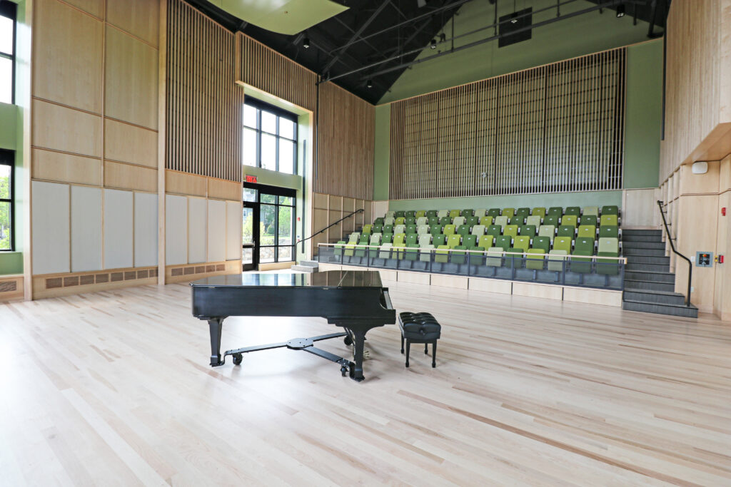 Recital room with sleek hardwood floors, a piano, and seats facing the piano and stage