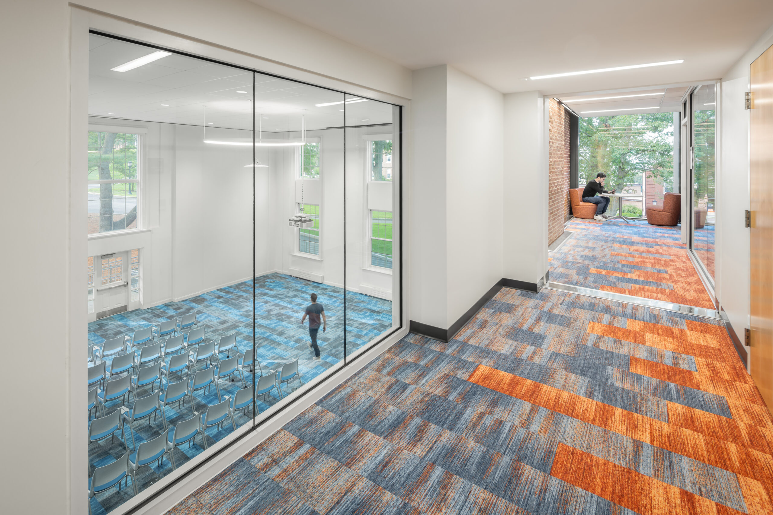 Tufts-EatonHall-Final-HiRes-8 Hallway overlooking an auditorium through large glass windows.